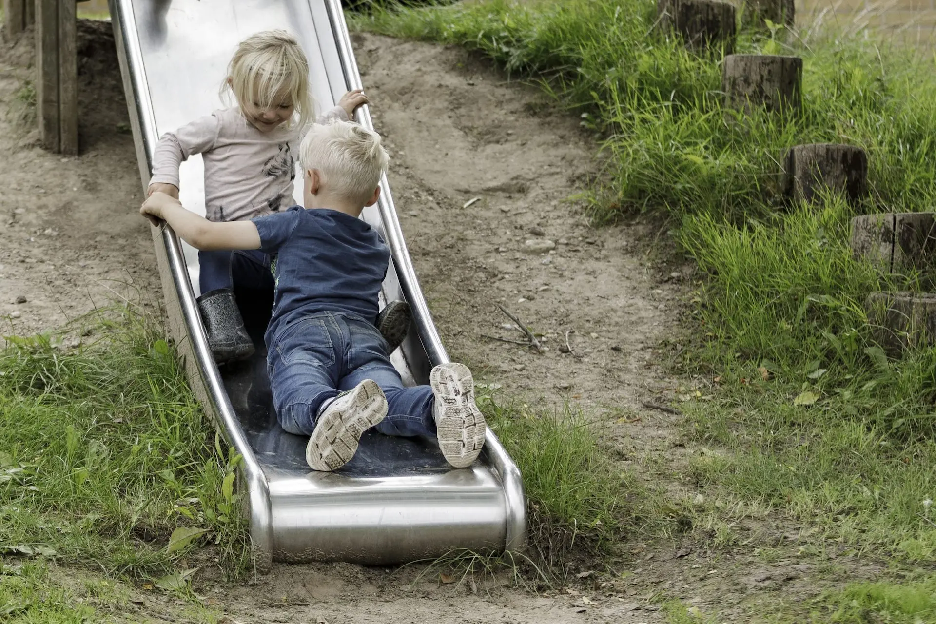 To børn suser ned ad rutsjebanen på legepladsen.